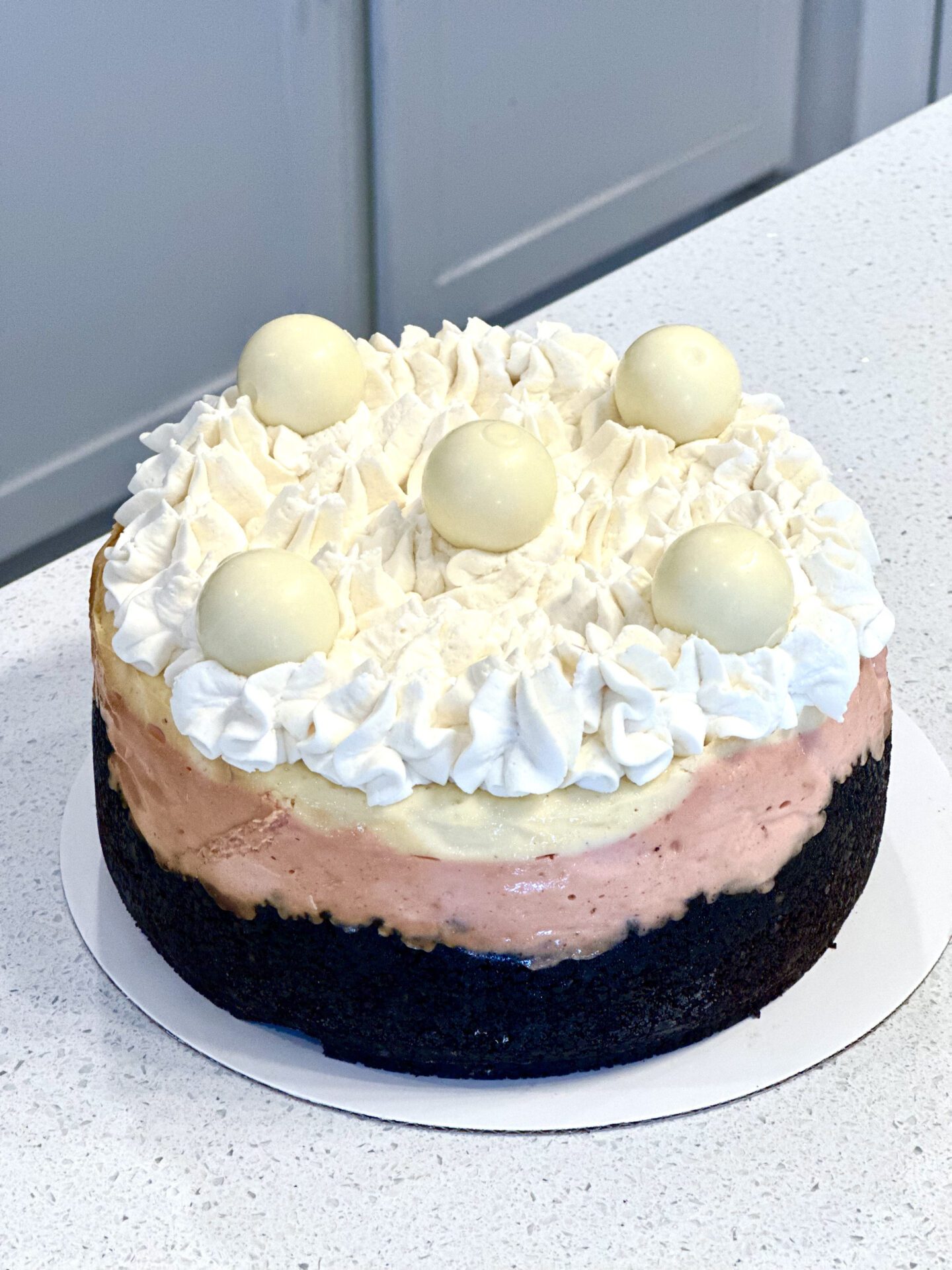 A round peach cobbler cheesecake on a blue plate, topped with whipped cream swirls, peach slices, and a crumbly streusel coating. The cheesecake has a light brown crust and is placed on a white countertop.